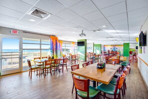 A spacious dining area with multiple tables and chairs, a large window with a view, and an exit sign. - Bay Watch Resort 1519 (North Myrtle Beach)