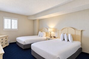 A hotel room with two beds, a dresser, a nightstand with a lamp, and a window with blinds. - Bay Watch Resort 1519 (North Myrtle Beach)