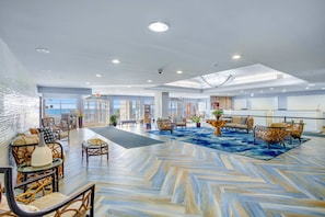 A spacious lobby with a herringbone floor pattern, seating areas with wicker furniture, and a view of the sea through large windows. - Bay Watch Resort 1519 (North Myrtle Beach)