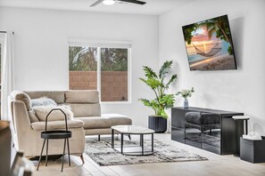A modern living room with a beige sofa, a coffee table, a potted plant, and a painting of a beach scene. - Modern 4BR · 10 Min to Strip, 8 Min to Airport (Las Vegas)