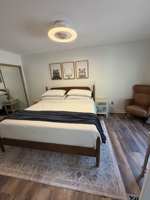 Ein Schlafzimmer mit einem Bett, Nachttischen, einem Sessel und Wandbildern.
