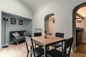 Un'area pranzo con tavolo, sedie, una bottiglia di vino e un bicchiere. Sullo sfondo, un divano e una lampada da terra.