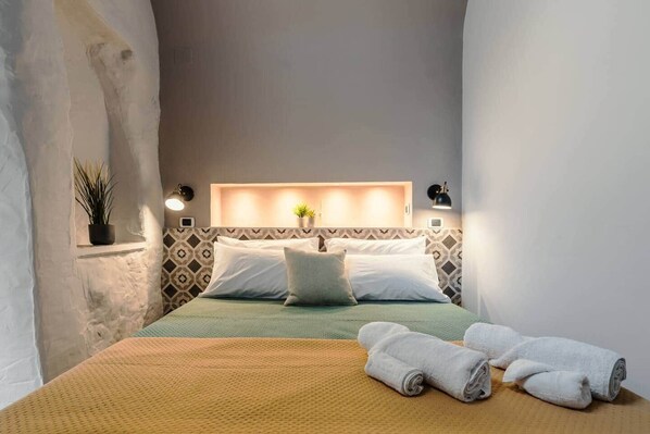 Ein Hotelzimmer mit einem Bett, Kissen, einer Nachttischlampe, einer kleinen Pflanze und gerollten Handtüchern auf dem Bett.
