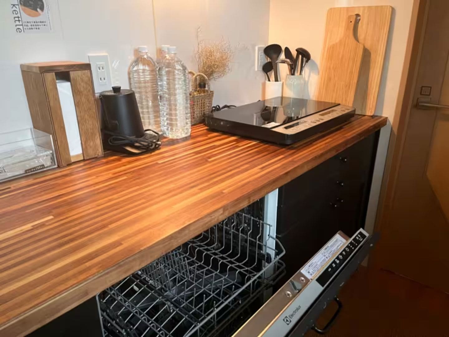 A kitchen with a wooden countertop, a dishwasher, and various kitchen items.