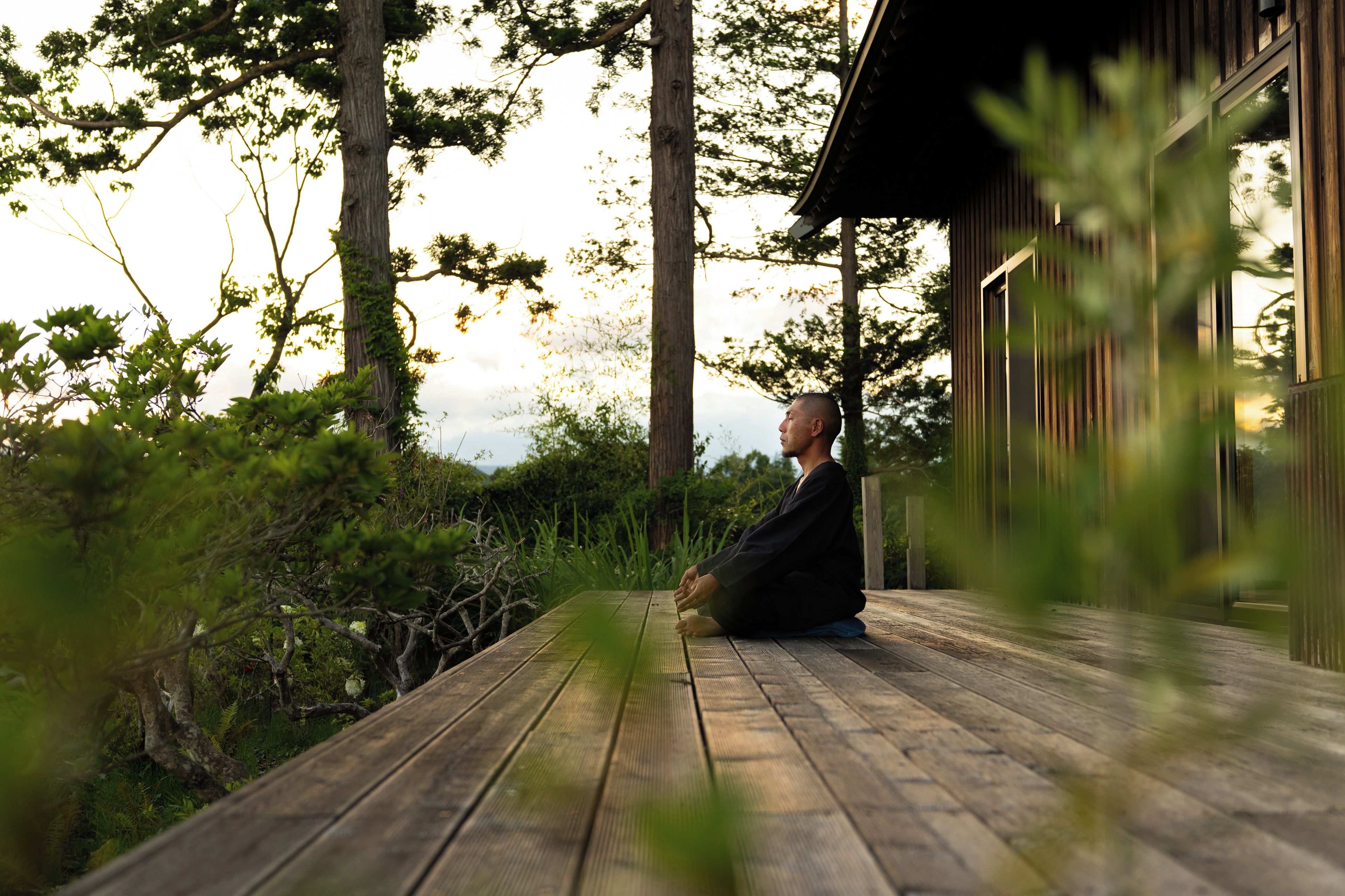 A person sitting on a wooden deck with a view of a building and trees in the background.