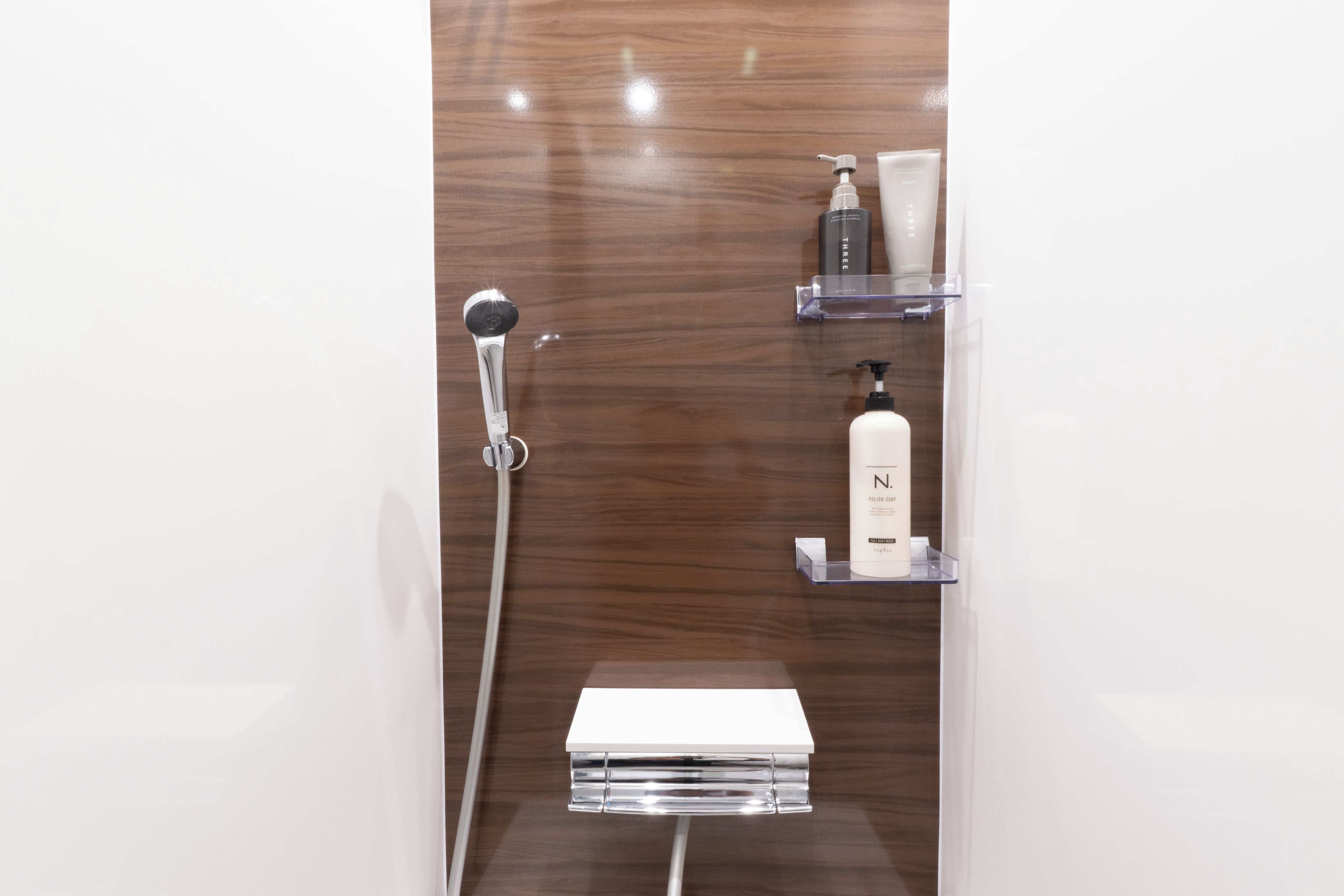 A modern bathroom with a wooden vanity, a shower, and toiletries on shelves.