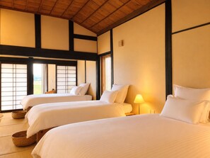 Una tradizionale stanza in stile giapponese, con pavimento in tatami, due letti con biancheria bianca e vista attraverso delle porte scorrevoli shoji.