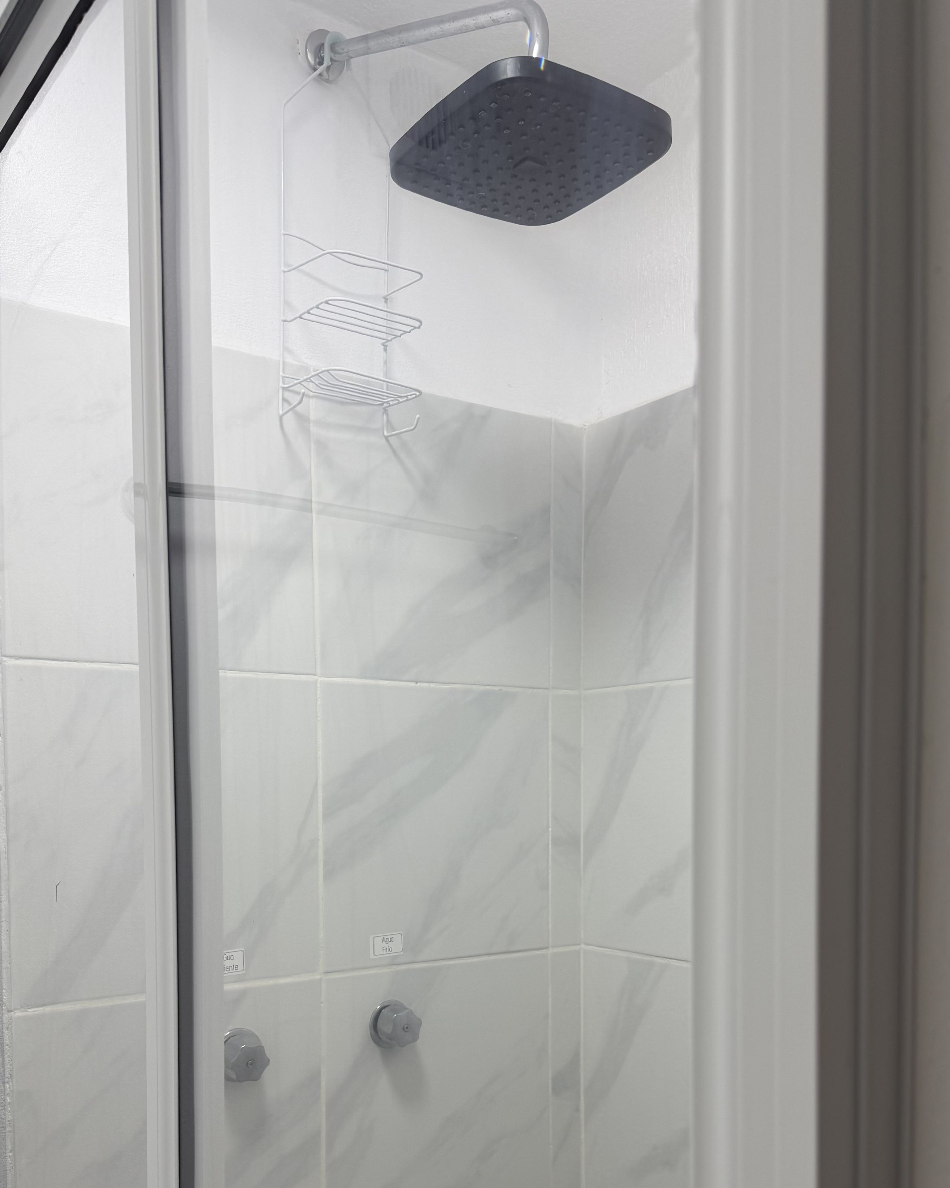 A shower with a handheld showerhead, a wall-mounted shelf, and a control knob.