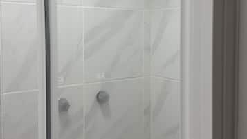 A shower with a handheld showerhead, a wall-mounted shelf, and a control knob.