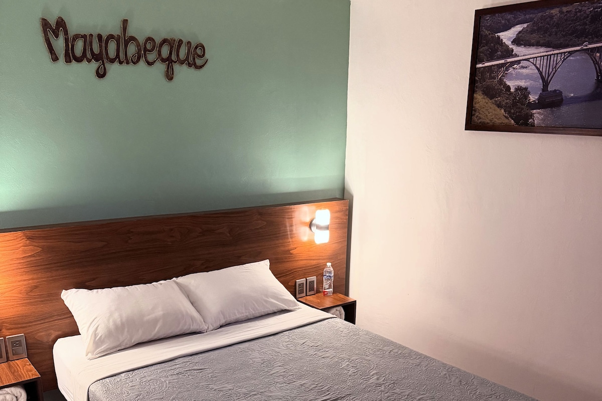 Una cama bien tendida con una colcha estampada, un cabecero de madera y una lámpara de pared.