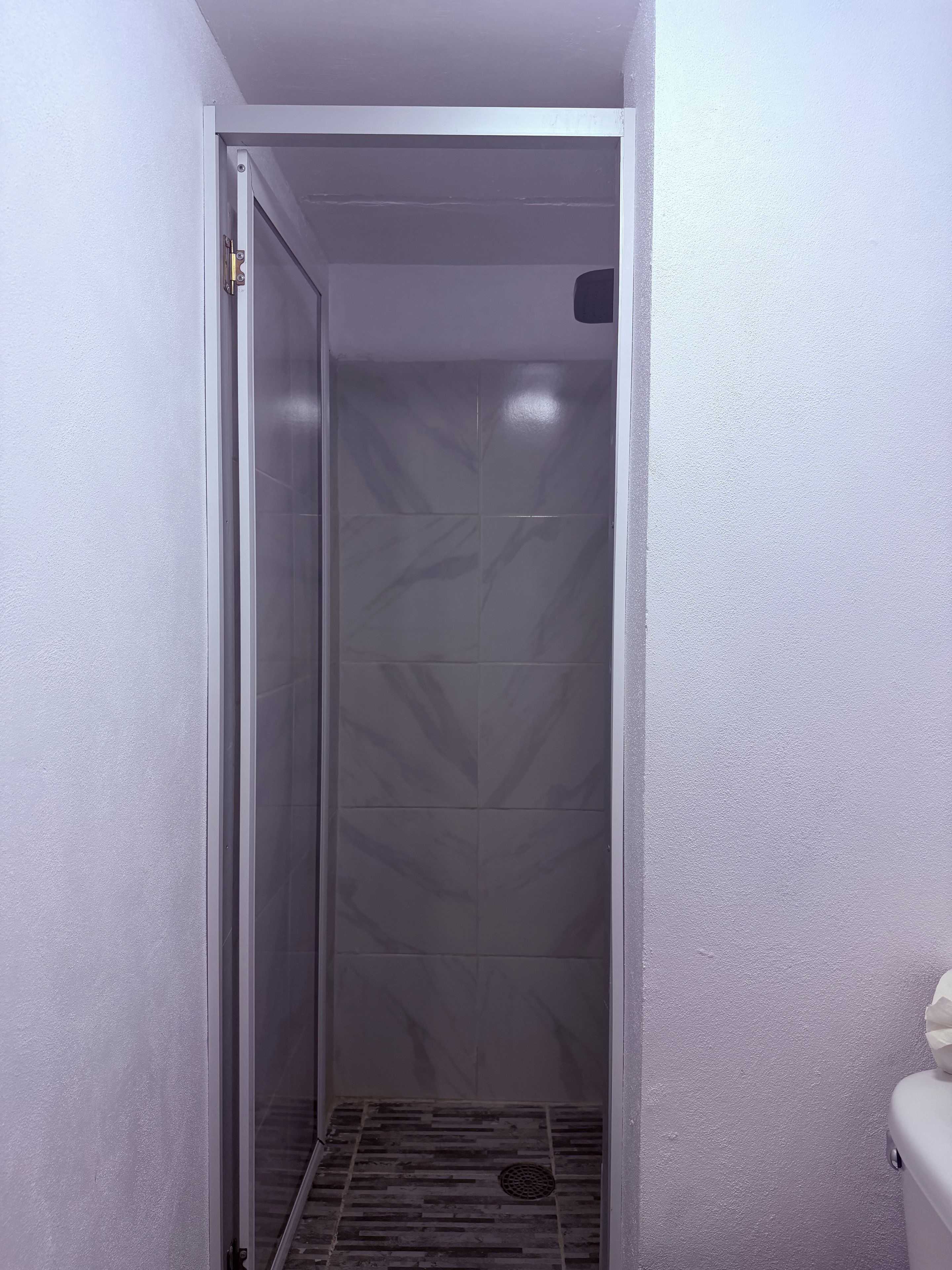 Un espace étroit et fermé, doté d’un sol carrelé et d’une porte avec une poignée en métal.