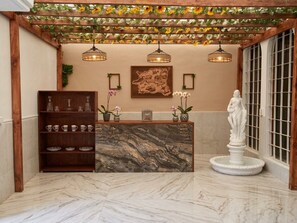 Un área de recepción con mostrador de mármol, una estantería de madera con cristalería, una estatua y un mapa en la pared.