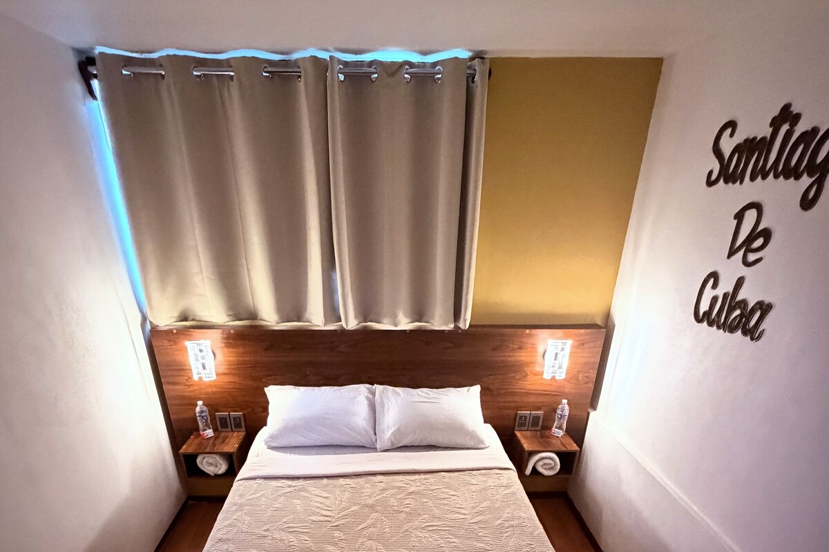Una habitación de hotel con cama, cortinas, lámparas de noche y una pared con un letrero.