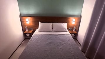 A hotel room with a bed, two bedside tables, a headboard with the name 'Villa Clara' on it, and a curtain on the right side.