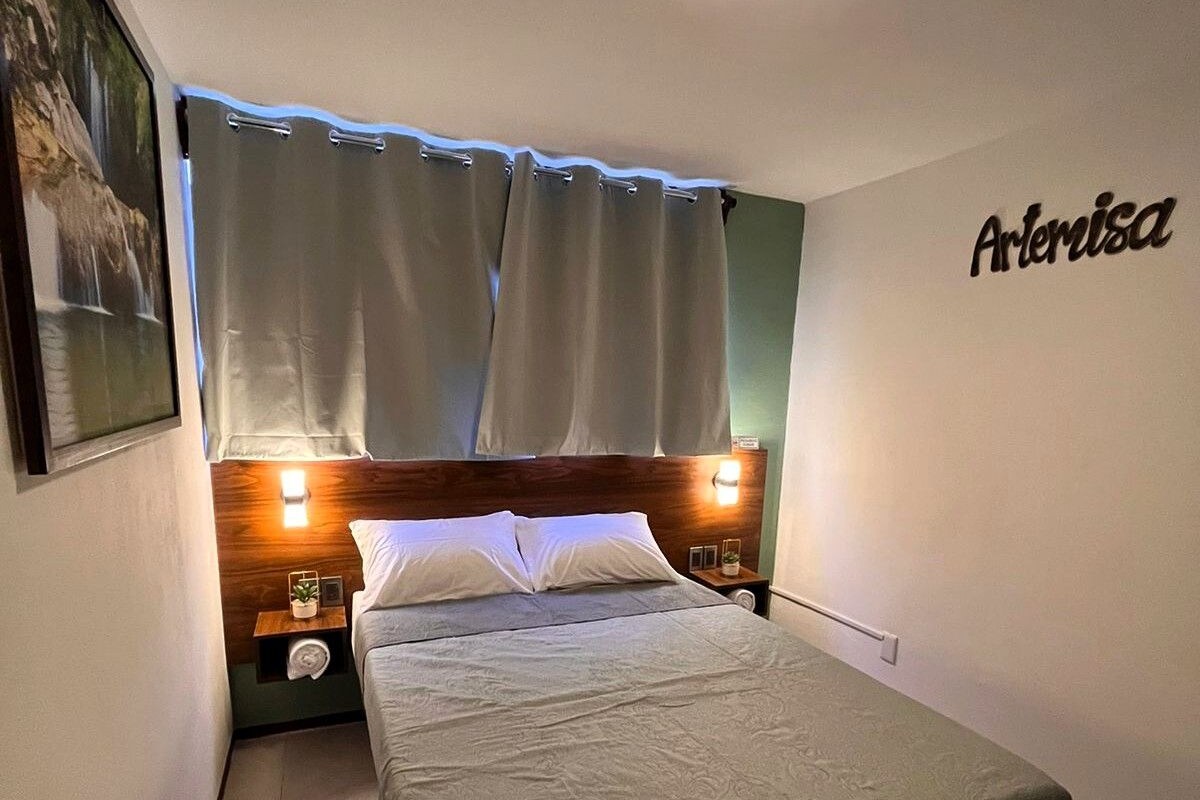 Habitación individual con una cama de una sola plaza, cabecera de madera, dos lámparas de noche, una mesita de noche y una obra de arte colgada en la pared.