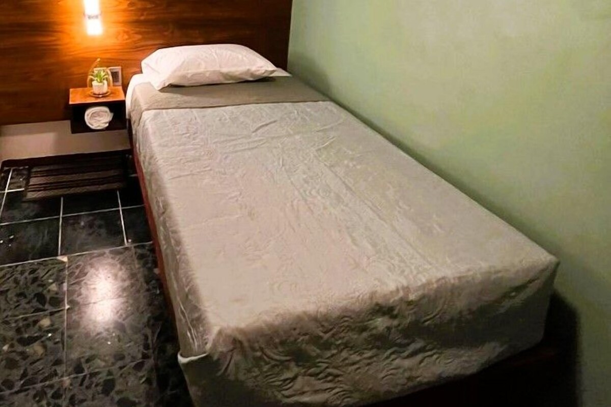Una cama individual con cabecera, una mesita de noche con lámpara y una pared con el nombre 'Malanga' en la esquina.
