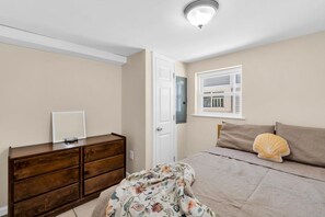 Ein Schlafzimmer mit Bett, Kommode, Tür und Fenster.