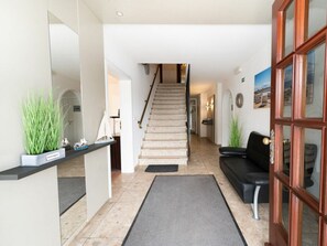 Ein Empfangsbereich mit einer Treppe zu den oberen Stockwerken, einem schwarzen Ledersofa und einer Holztür mit Glasfeldern.