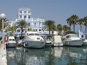 A marina with several yachts docked, a large building with a tower, and palm trees in the background. - Charming apartment in Estepona old town (Estepona)