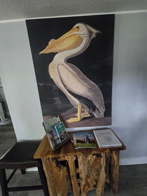 A wooden table with a large pelican painting, a directory, and a guest book. - Mane Wave's Space Coast Retreat (Cocoa)