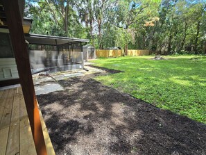 Ein Garten mit überdachter Terrasse, einer Holzterrasse und einem umzäunten Bereich.