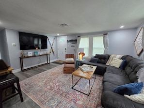 A living room with a television, a sofa, a coffee table, and a patterned rug. - Mane Wave's Space Coast Retreat (Cocoa)