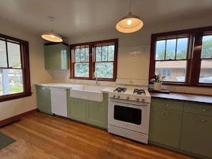 A kitchen with a white stove, green cabinets, and wooden flooring.