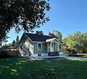 A single-story house with a front porch, a chimney, and a fenced backyard.