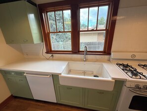 A kitchen with a window, sink, stove, and green cabinets.