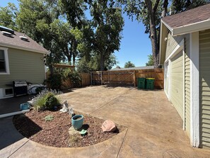 A backyard with a patio, a barbecue grill, a wooden fence, and a garage.