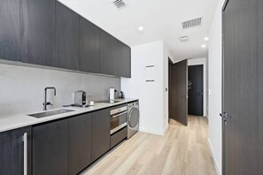 A modern kitchen with dark cabinetry, a built-in dishwasher, and a coffee maker. - Downtown Miami Studio at E11EVEN | 24th Floor (Miami)