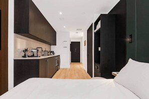 Ett modernt hotellrum med en säng, ett litet kök och ett separat badrum.