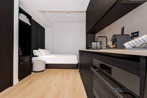 A compact hotel room with a bed, a small kitchenette, a dark wardrobe, and a trash bin. - E11EVEN Skyline Studio | 33rd Floor City Views (Miami)