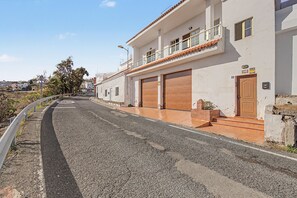 Un carrer residencial amb una casa de dos pisos, un balcó, un garatge i una entrada de cotxes.