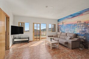 Ein Wohnzimmer mit Flachbildfernseher, einer Couch, einem Couchtisch und einer Wandmalerei mit Stadtansicht.