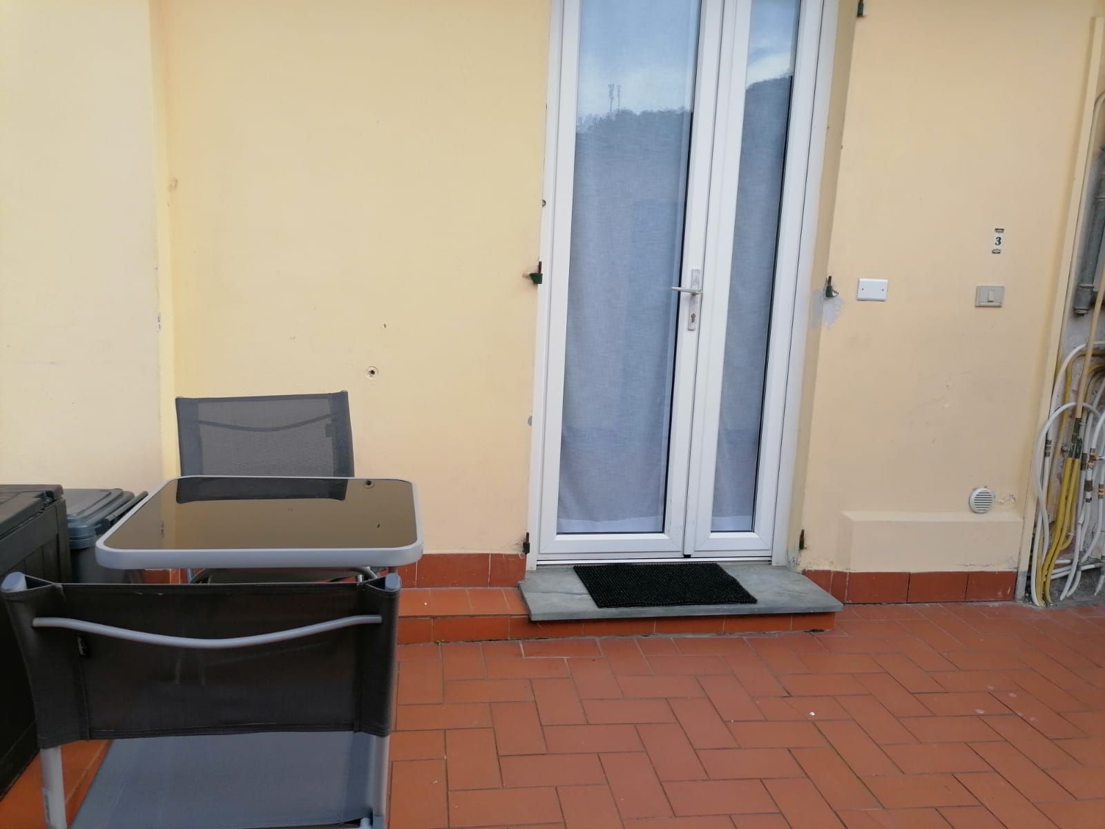 Een terras buiten met een tafel, stoelen, een schuifpui en een klein opstapje naar een deur.