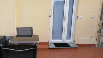 Een terras buiten met een tafel, stoelen, een schuifpui en een klein opstapje naar een deur.
