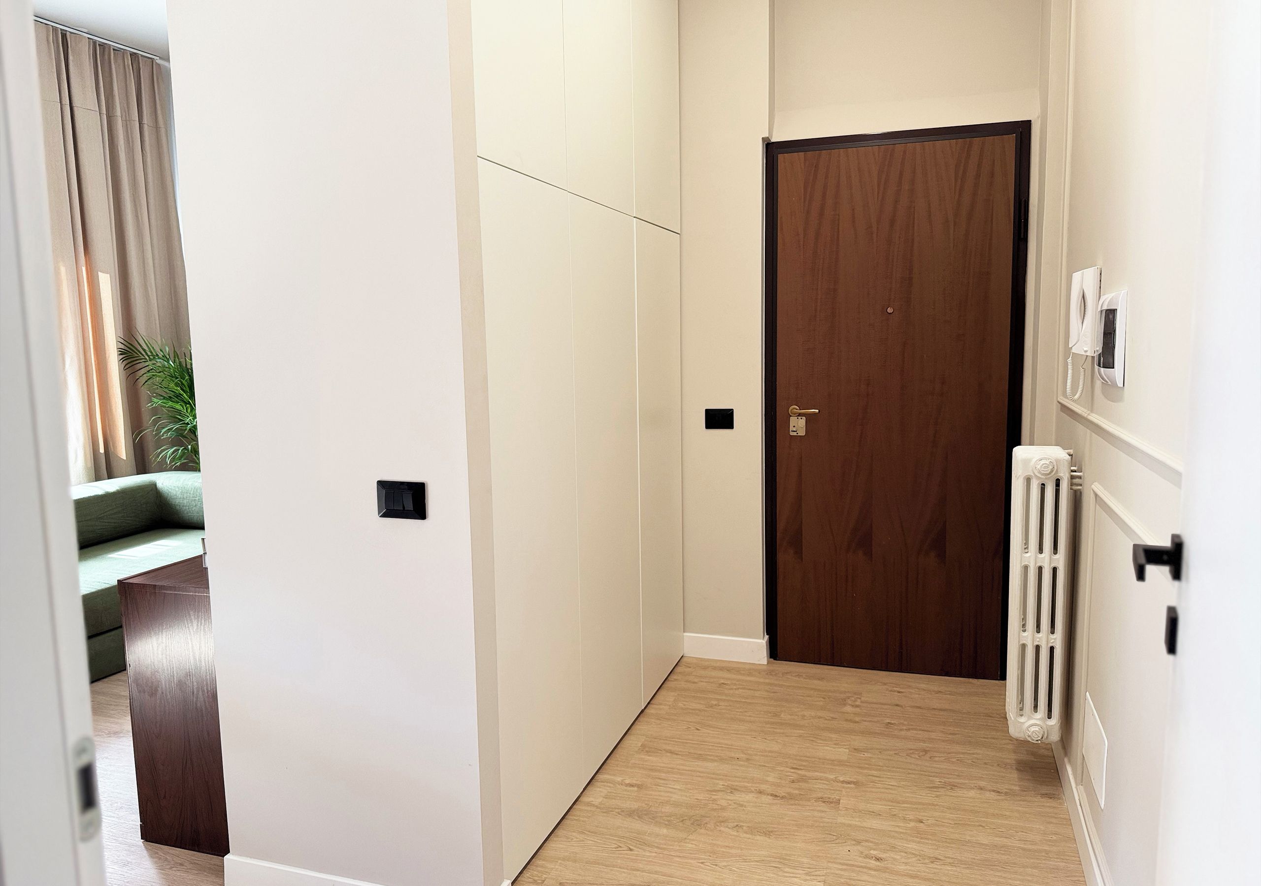Ein Korridor mit einer Holztür, einem Heizkörper und einem Lichtschalter an der Wand.
