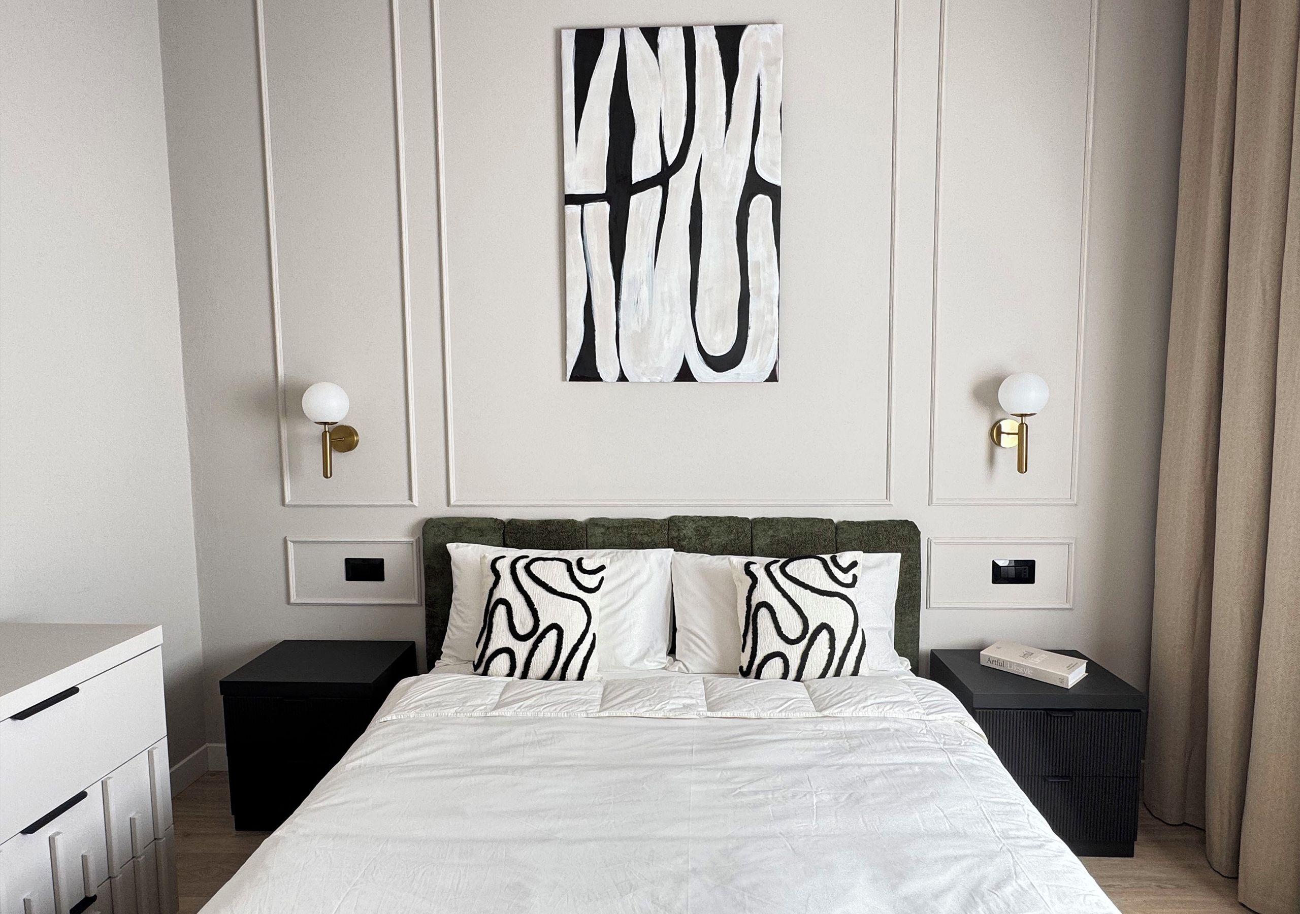A hotel room with a bed, two bedside tables, a nightstand, a wall-mounted artwork, and a window with curtains.