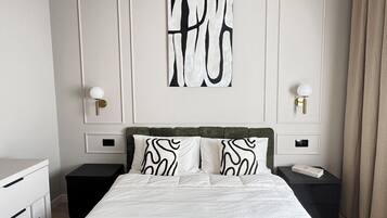 A hotel room with a bed, two bedside tables, a nightstand, a wall-mounted artwork, and a window with curtains.