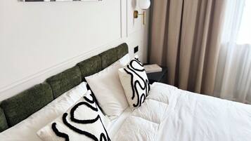 A neatly made bed with white bedding and a green headboard, a bedside table with a lamp, and a painting on the wall.