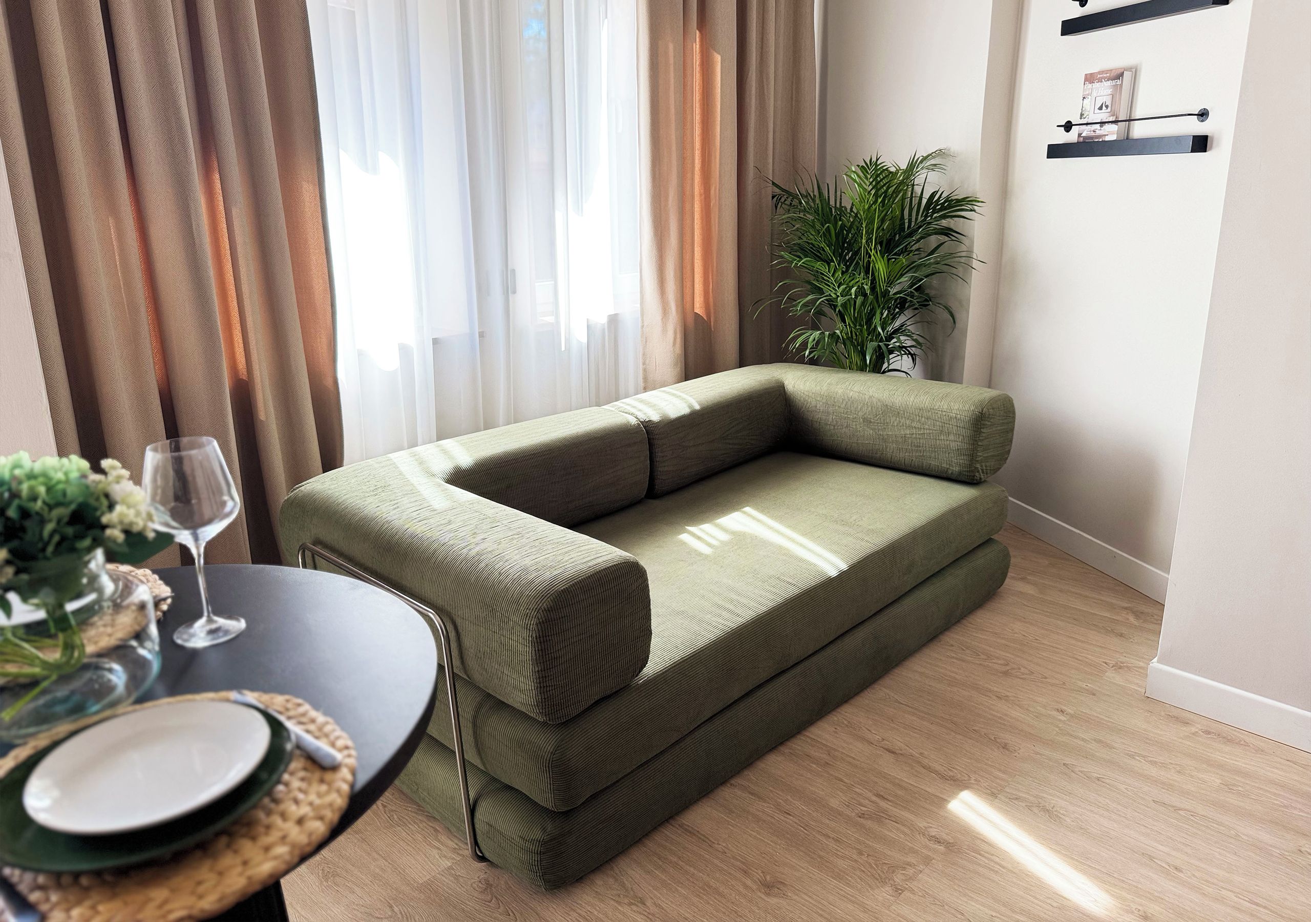 Un salon moderne avec un canapé vert, une table à manger avec un plateau en verre et une plante en pot.