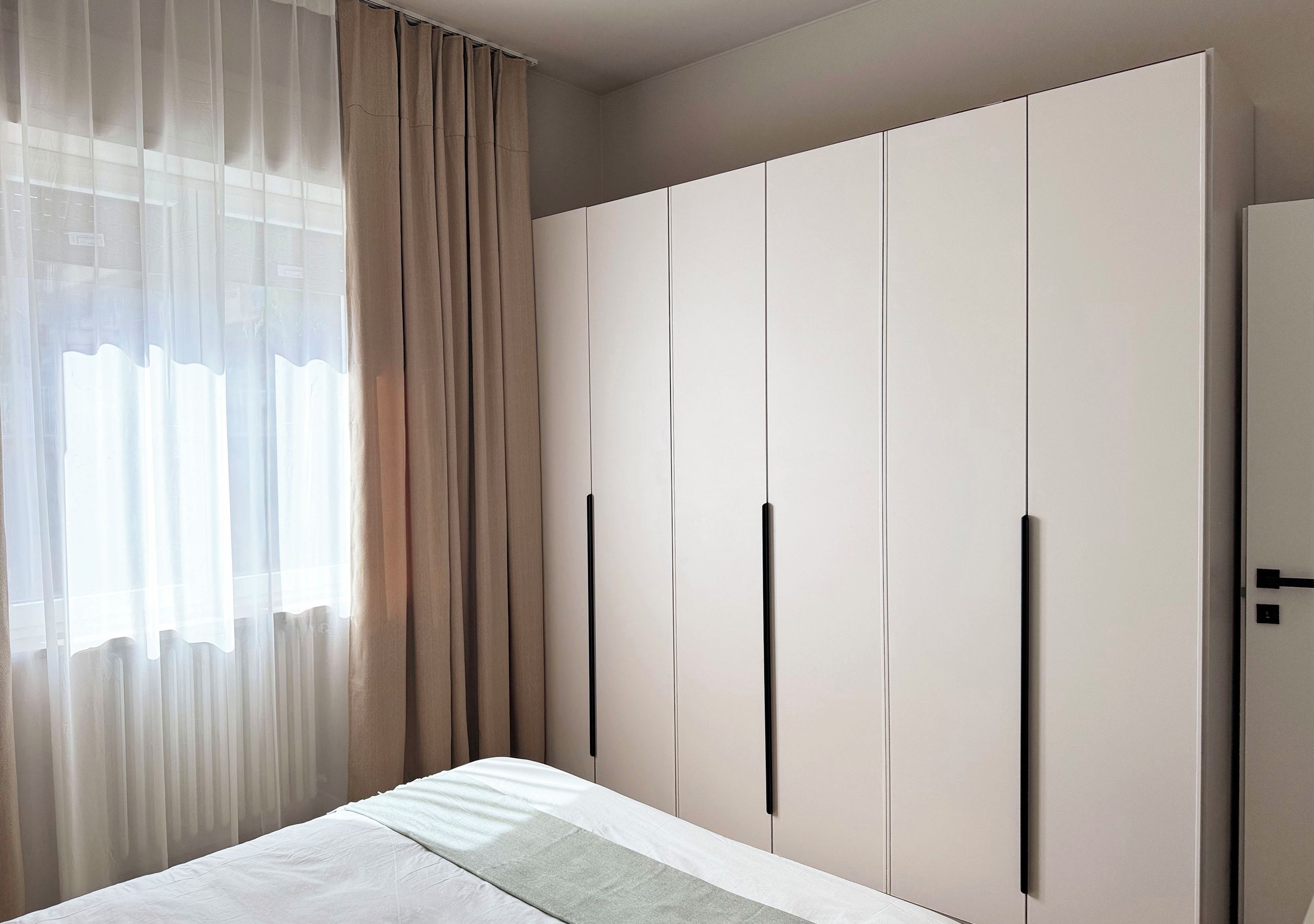 Ein Schlafzimmer mit Bett, Kleiderschrank und durchsichtigen Vorhängen.