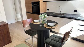 A modern kitchen with a dining area, featuring a round table with chairs, a vase with flowers, and a black countertop.