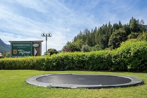 Une enseigne verte indiquant un restaurant et un hôtel, un trampoline installé sur une pelouse, et une forêt dense en arrière-plan.