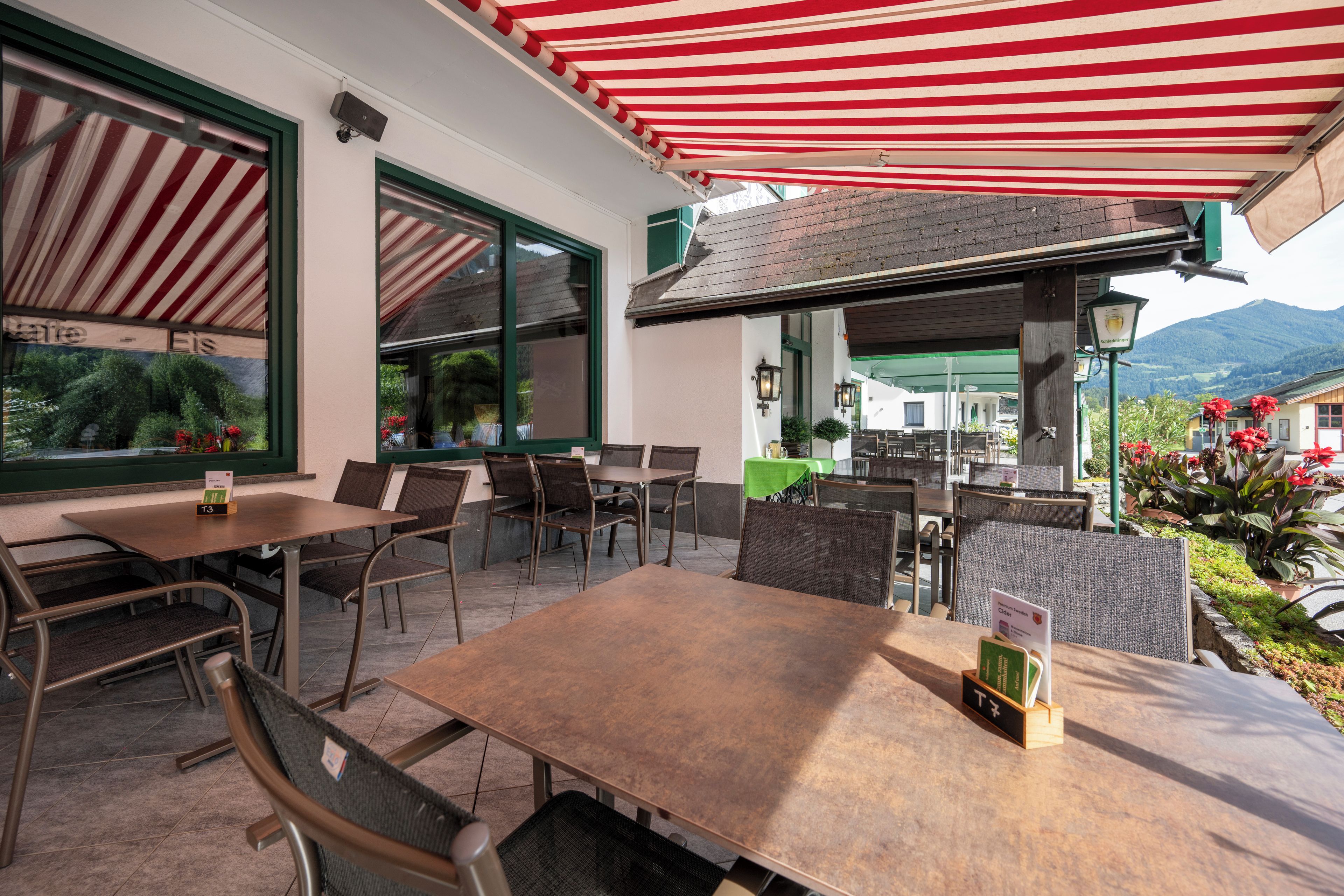 An outdoor seating area with tables and chairs, a red and white striped awning, and a view of a mountain in the background.