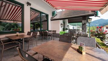 An outdoor seating area with tables and chairs, a red and white striped awning, and a view of a mountain in the background.
