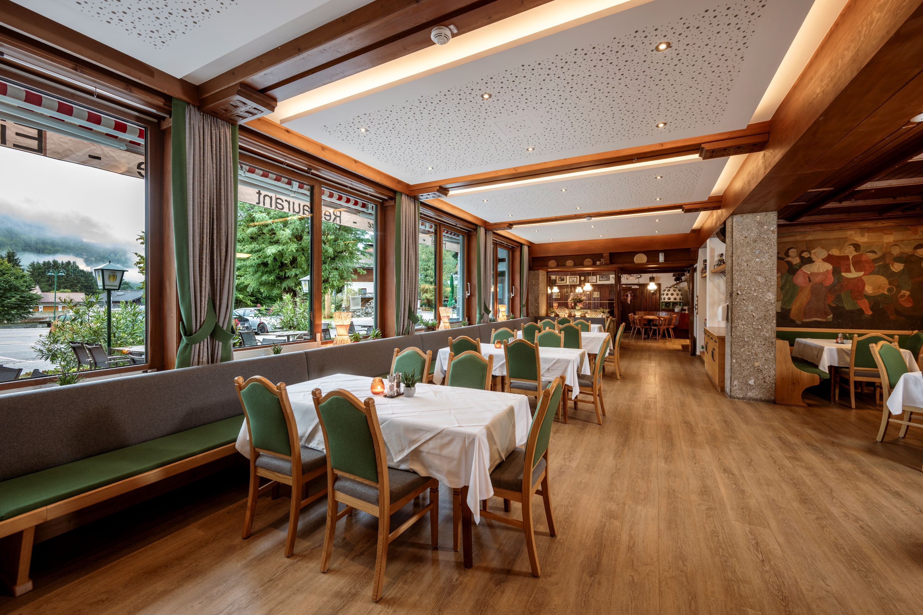 Un restaurant doté de planchers en bois, de sièges rembourrés de couleur verte et de grandes fenêtres offrant une vue sur l’extérieur.
