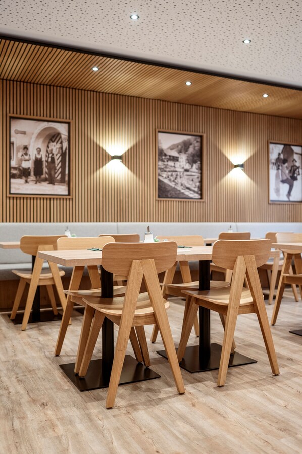 L’intérieur d’un restaurant présente des tables et des chaises en bois, des spots encastrés au plafond et des photographies en noir et blanc encadrées qui ornent les murs.