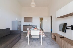 Un espace de vie compact comprenant un coin repas, une kitchenette et un téléviseur fixé au mur.